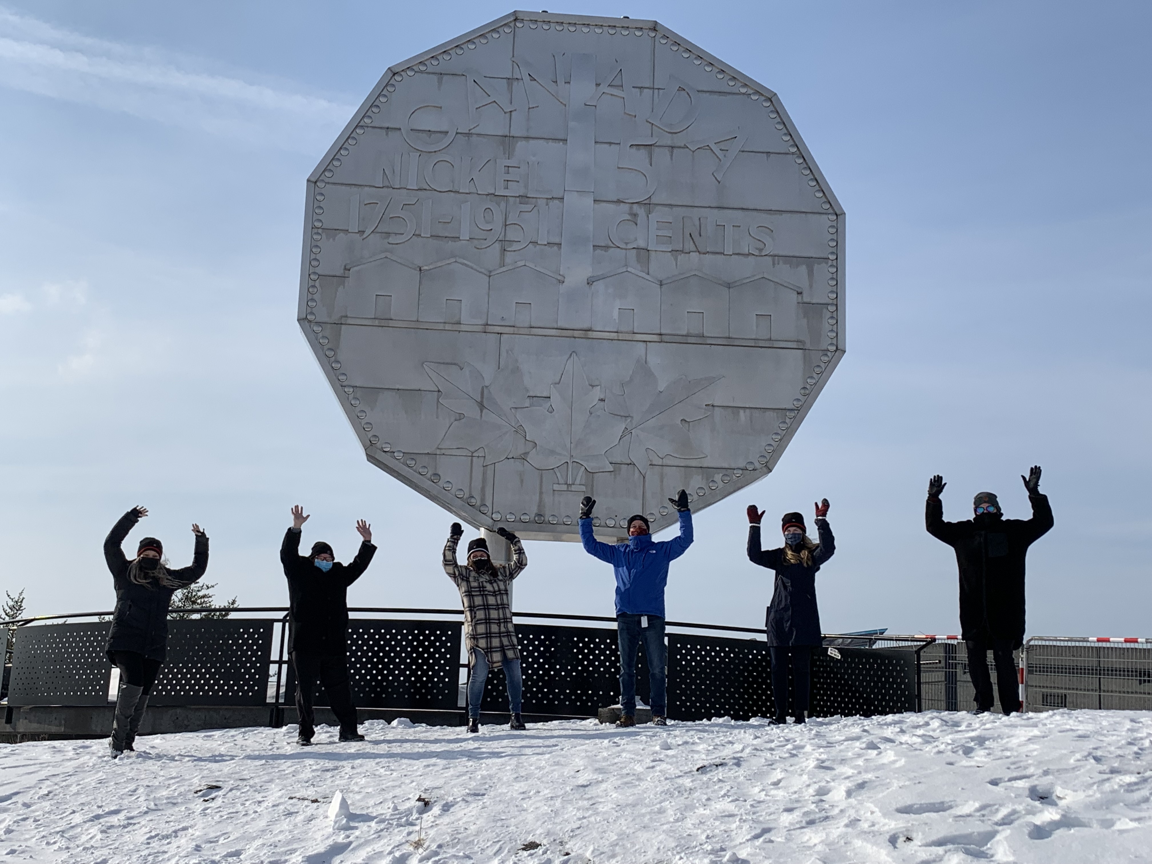 staff standing in front of big nickel with hands in the air