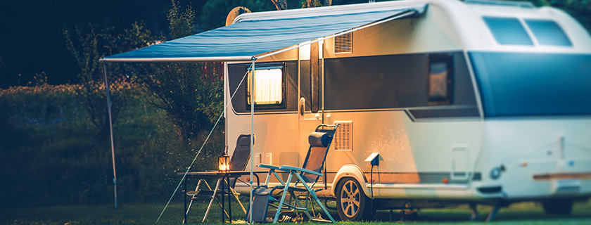 A recreational vehicle with an awning and lawn chairs underneath it.
