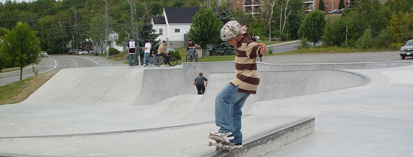 A young boy on a skateboard doing a trick at the skate park with a group of boys on bikes in the background.