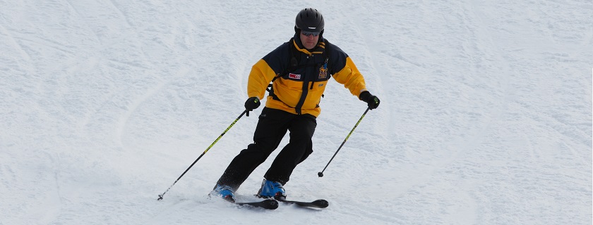 A man skiing down a ski hill in deep snow with a chair lift in the background.
