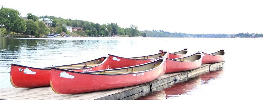 Five red kayaks laid down on a wooden dock by the water.