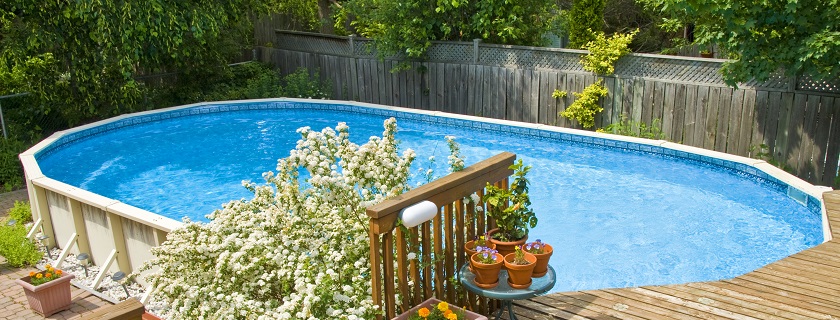 A pool with a deck and trees surrounded by a fence.