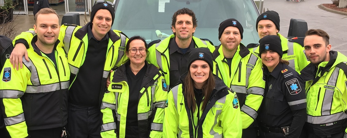 Six male paramedics and three female paramedics in their uniforms smiling.